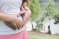 Young asian woman and her husband together caressing her pregnant belly holding their hands in a heart shape on her baby bump. Pr Royalty Free Stock Photo