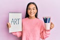 Young asian woman holding art notebook and colored pencils smiling with a happy and cool smile on face Royalty Free Stock Photo