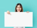 Young Asian woman holding blank paper with smiling face and looking on the blue background. for advertising signs. Royalty Free Stock Photo