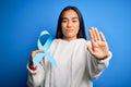 Young asian woman holding blue cancer ribbon symbol standing over isolated background with open hand doing stop sign with serious Royalty Free Stock Photo