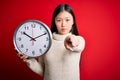 Young asian woman holding countdown big clock over red isolated background pointing with finger to the camera and to you, hand Royalty Free Stock Photo