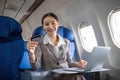 Young Asian woman holding credit card shopping online using website on laptop Sitting near window in first class on Royalty Free Stock Photo