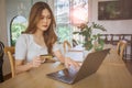 Young Asian woman holding credit card and using laptop computer. Beautiful happy young girl in cafe. Online shopping, E-commerce, Royalty Free Stock Photo