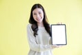 Young asian woman holding digital tablet with blank screen for mock up, template, smiling while standing over isolated yellow Royalty Free Stock Photo