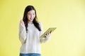 Young asian woman holding digital tablet , smiling while standing over isolated yellow background Royalty Free Stock Photo