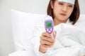 Young Asian woman holding digital thermometer with high fever while sleeping on white bed at home.