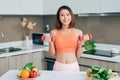 Young Asian woman holding dumbell and wearing sportive clother in kitchen