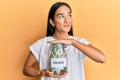 Young asian woman holding jar with savings smiling looking to the side and staring away thinking Royalty Free Stock Photo