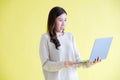 Young asian woman holding laptop computer, smiling and looking at camera while standing over isolated yellow background Royalty Free Stock Photo