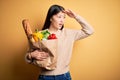 Young asian woman holding paper bag of fresh healthy groceries over yellow  background very happy and smiling looking far Royalty Free Stock Photo