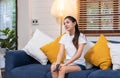 Young asian woman holding remote control and enjoy watching tv in living room at home,sitting on sofa Royalty Free Stock Photo