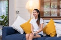 Young asian woman holding remote control and enjoy watching tv in living room at home,sitting on sofa Royalty Free Stock Photo