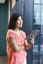 A young Asian woman holding a tablet and looking away in a modern business office