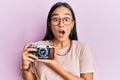 Young asian woman holding vintage camera afraid and shocked with surprise and amazed expression, fear and excited face Royalty Free Stock Photo