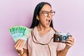 Young asian woman holding vintage camera and 200 russian ruble banknotes angry and mad screaming frustrated and furious, shouting Royalty Free Stock Photo
