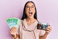 Young asian woman holding vintage camera and 200 russian ruble banknotes angry and mad screaming frustrated and furious, shouting Royalty Free Stock Photo