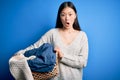 Young asian woman holding wicker laundry basket doing domestic chores scared in shock with a surprise face, afraid and excited