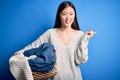 Young asian woman holding wicker laundry basket doing domestic chores very happy pointing with hand and finger to the side
