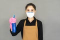 Young asian woman housewife in brown apron and pink gloves wore medical face mask,Cleaning spay bottle on hands isolated on gray