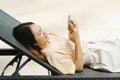 A young Asian woman with long hair lies on her mobile phone chatting with her friend on a beach chair by the pool on the weekends. Royalty Free Stock Photo