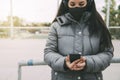 Young asian woman looking at cellphone wearing headphones and protective face mask. Copy space