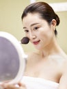 Young asian woman looking in the mirror while applying make-up Royalty Free Stock Photo