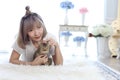 A young Asian woman lounging with a cat in a living room with a white fur rug. Woman and cat looking forword