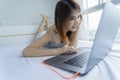 Young asian Woman lying in bed with laptop smiling relaxing in bed room. Stay home, Work from home concept Royalty Free Stock Photo