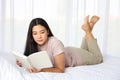 Young Asian woman lying down on the bed while reading a book in cozy and relax feeling Royalty Free Stock Photo