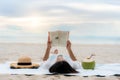 Young Asian woman lying on a tropical summer beach sea for relax reading book with coconut juice beside her. Summer, holidays, Royalty Free Stock Photo