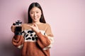 Young asian woman making a glass of coffe using french press coffee maker over pink background very happy pointing with hand and