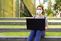 Young Asian woman with mask for protection from corona virus outbreak using laptop while sitting outdoors Royalty Free Stock Photo