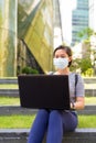 Young Asian woman with mask for protection from corona virus outbreak using laptop while sitting outdoors Royalty Free Stock Photo