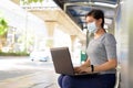 Young Asian woman with mask using laptop while sitting at the bus stop Royalty Free Stock Photo