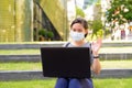 Young Asian woman with mask video calling using laptop while sitting on the stairs outdoors Royalty Free Stock Photo