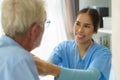 Young Asian woman nurse helping get dress to disabled elderly man in bed at retirement home. Millennial caregiver assisting Royalty Free Stock Photo