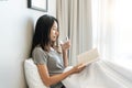 Asian woman in pajamas drinking water while reading a book sitting on the bed in the morning. Healthy lifestyle concept Royalty Free Stock Photo