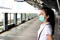 Young Asian woman passenger wearing medical hygiene protective face mask standing in sky train station in big city