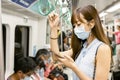 Young Asian woman passenger wearing surgical mask and listening music via mobile phone in subway train