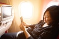Young asian woman on  plane with smartphone in her hands..Play cell phone on board in airplane near window seat Royalty Free Stock Photo