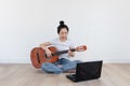 Young Asian woman play guitar, with computer laptop in living room