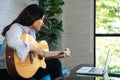 Young Asian woman practicing and learning how to play guitar on laptop computer monitor. Female guitarist watching Royalty Free Stock Photo