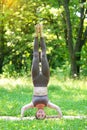 Young asian woman practicing yoga outdoors, doing headstand pose.