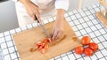 Young Asian woman is preparing healthy food vegetable salad by Cutting tomato for ingredients on cutting board on light kitchen, Royalty Free Stock Photo