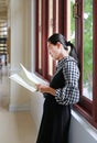 Young asian woman reading book near windows in the library Royalty Free Stock Photo