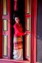 Young Asian woman with red Thai Lanna traditional dress stand at door with red color and old style of ancient house also look at Royalty Free Stock Photo