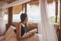 Young asian woman resting and reading a book on the bed in thatched hut among the mountain on vacation Royalty Free Stock Photo