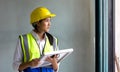 Young asian woman in a safety vest and hardhat holding solar cell panel while looking out of the window. Work environment of Royalty Free Stock Photo