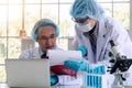 Woman and senior man researcher scientist with laptop, lab coat, gloves and eyeglasses analyzing experiment together Royalty Free Stock Photo