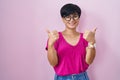 Young asian woman with short hair standing over pink background success sign doing positive gesture with hand, thumbs up smiling Royalty Free Stock Photo